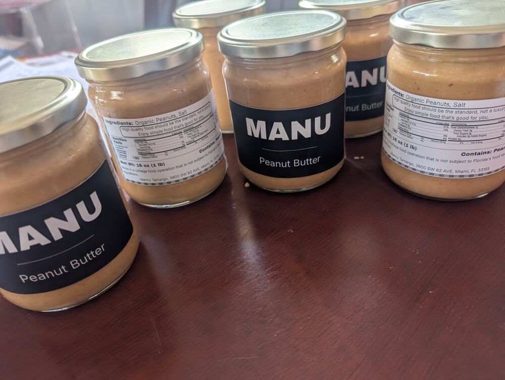 Four glass jars of MANU peanut butter on a wooden table.